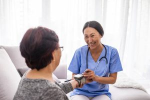 Happy senior woman having her blood pressure measured in a nursing home by her caregiver